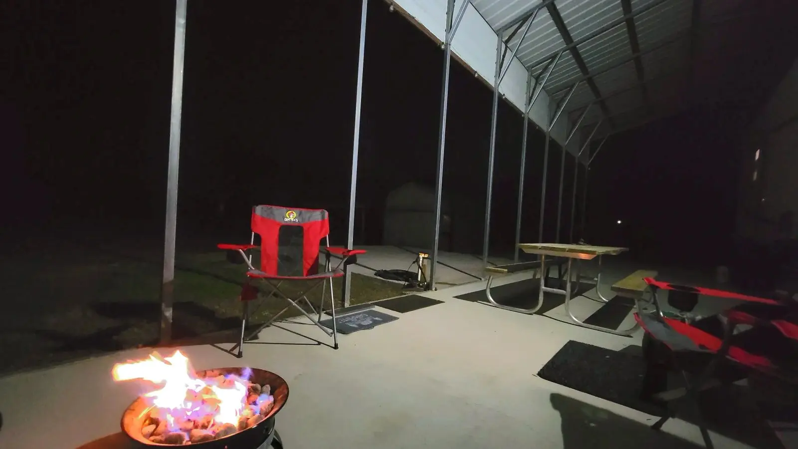 The covered patio at night with seating for four and a propane fire pit.