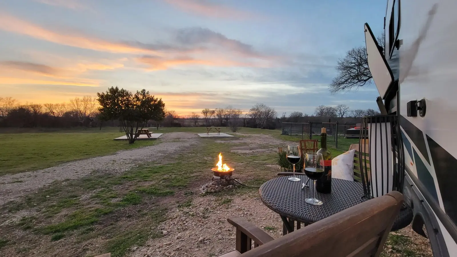 Image of sitting-area by the River RV with wine glasses on the table and propane fire pit lit.
