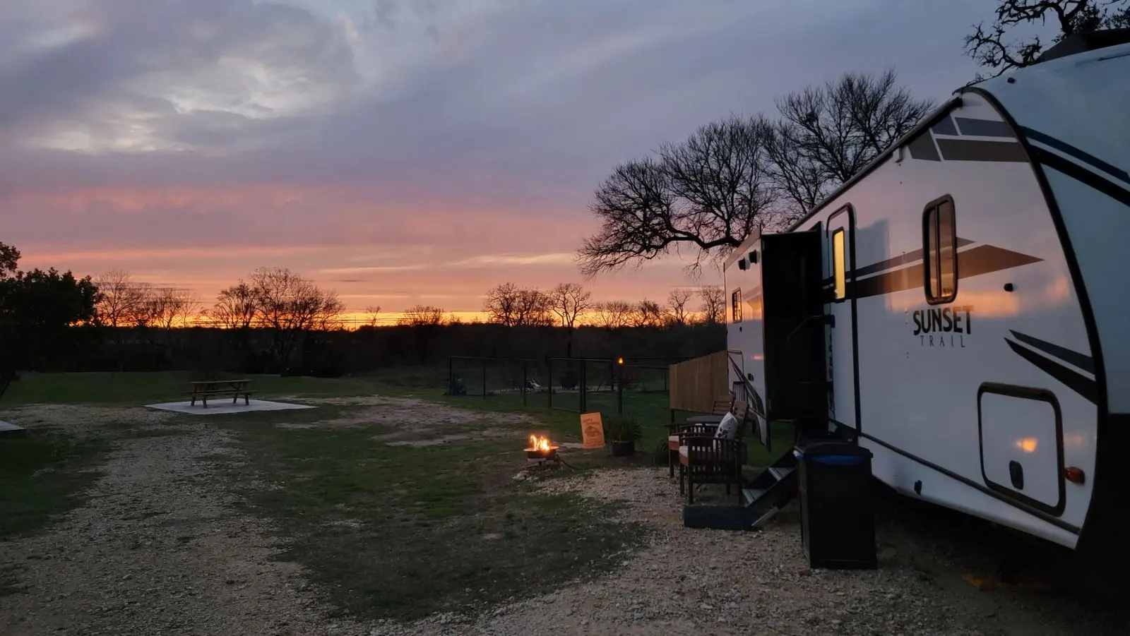 Image of the steps up to the River RV, the sitting area, the propane fire pit lit as the sun sets.